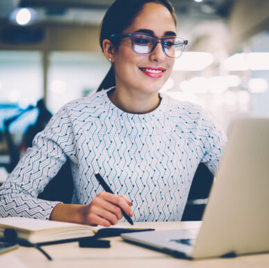 Smart young woman satisfied with learning language during online courses using netbook, smiling female student doing homework task in college library searching information via laptop computer